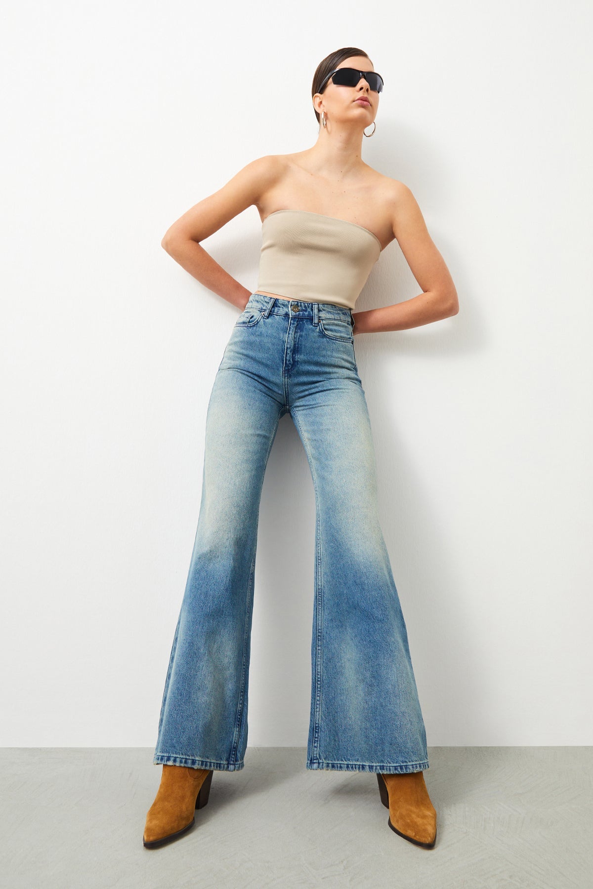 Casual chic: Woman styles AWE Vintage jeans with boots and a bandeau top of a chic summer outfit.