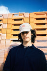 Young man wearing CREST baseball cap in beige with orange logo, styled withdraw blue shirt.